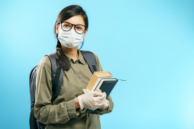 portrait-female-student-medical-protective-mask-gloves-holding-books-blue-background_97780-669